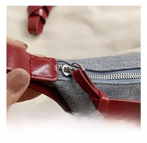 Detail view of denim underarm bag showing silver metal zipper and red leather accents