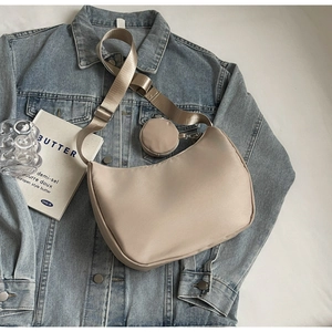 Beige nylon crescent bag with wide strap and round coin purse on denim jacket