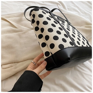 Close-up of a polka dot tote bag with leather handles and a gold logo on white fabric