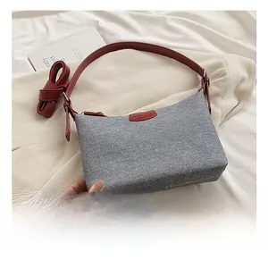 Detail showing the gray twill fabric underarm bag with red leather strap and logo patch