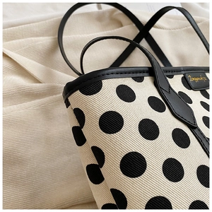 Close-up of polka dot canvas tote with black leather trim and golden brand plaque