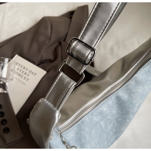 Detail of denim and silver leather patchwork bag with adjustable metal buckle strap