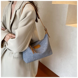 Detail of light blue textured shoulder bag with brown leather strap and decorative patch