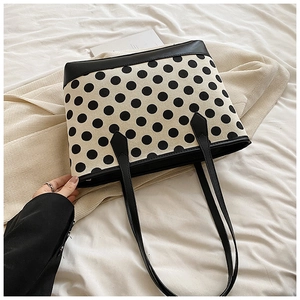 Detailed view of polka dot tote bag with black leather handles on white fabric