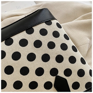 Close-up of canvas tote showing black polka dots and premium leather stitching detail
