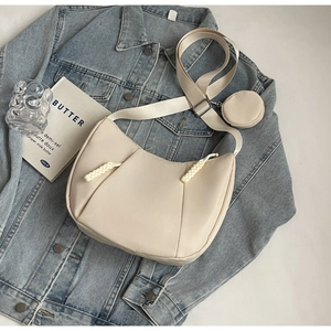 Detail of beige crescent crossbody bag with wide strap and round coin purse on denim
