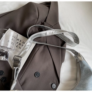 Detail of silver metallic hobo bag with adjustable buckle on brown blazer backdrop