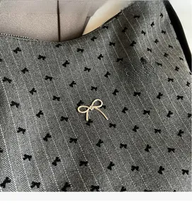 Detail of grey herringbone fabric with black bow print and silver metal bow pendant