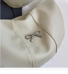 Detailed macro of silver bow hardware on cream pebbled leather crossbody bag