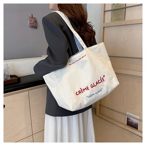 Close-up of canvas tote bag featuring embroidered Crème Glacée text and wide strap