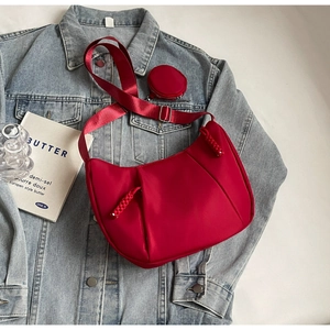Detail of red crescent bag with mini round pouch and adjustable woven strap on denim