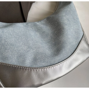 Detail of light blue denim and silver leather patchwork with fine stitching on shoulder bag