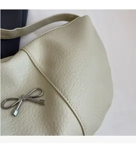 Detail of creamy white textured leather bag with a silver metal bow pendant decoration