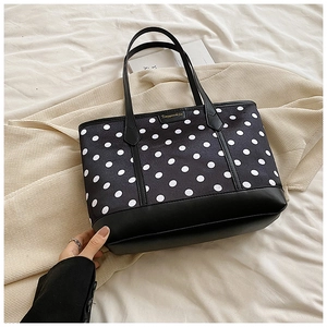 Chic black and white polka dot tote bag with leather straps on a beige cozy surface