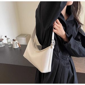 Detalle del bolso hobo de cuero blanco crema con hebilla plateada sobre vestido negro plisado
