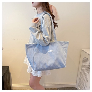 Detail of blue striped canvas tote bag with Magic Pocket tag worn on shoulder
