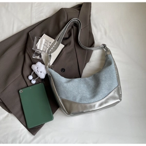 Detail of denim and silver patchwork crescent bag with plush cloud charm on white cloth