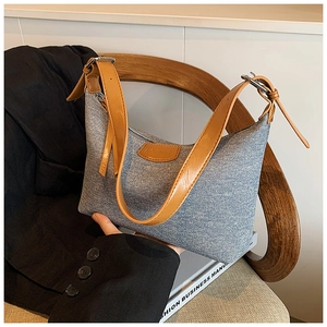Detail of hobo bag showing blue denim texture and brown leather strap on a wooden chair