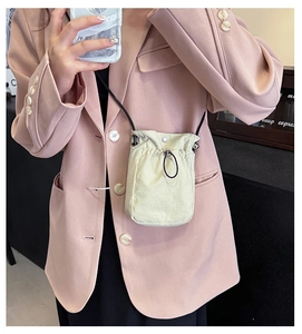 Detail of beige drawstring mini crossbody bag with black rope strap on casual outfit