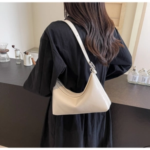 Model wearing a minimalist cream dumpling shoulder bag with adjustable strap at a bar