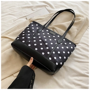 Detailed close-up of a black and white polka dot tote bag with premium metal logo detail