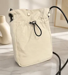Close-up of cream canvas mini crossbody bag with drawstring closure on denim fabric
