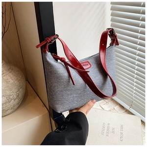Detail of blue denim underarm bag with red strap and decorative red oval logo plaque