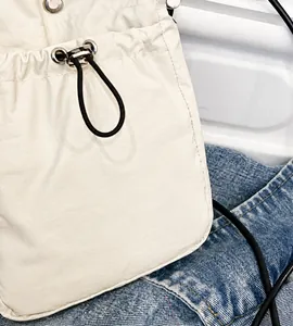 Close-up of off-white fabric crossbody bag with drawstring closure and black shoulder strap