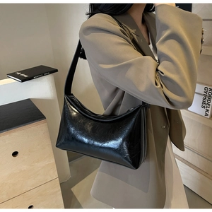 Detail of black glossy crescent bag with wrinkled patent leather texture and wide shoulder strap