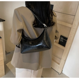 Close-up of black glossy leather hobo bag with silver metallic buckle on model shoulder