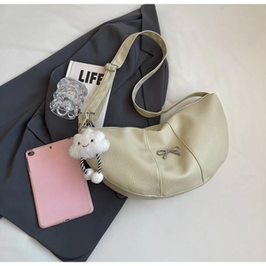 Detail of beige crescent bag with metal bow and cloud charm on a grey blazer background