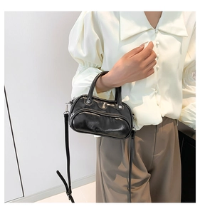 Detail of glossy black crossbody bag with silver hardware held by model in hand