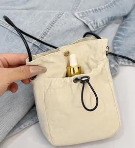 Close-up of cream nylon crossbody bag featuring a functional front pocket and drawstring