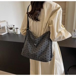 Detail of grey bow-print tote bag with metal ribbon buckle shown on model's shoulder