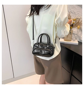 Detail of a black glossy crossbody bag with silver hardware and front zipper pocket