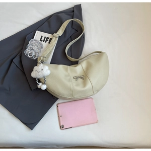 Detail view of beige crescent bag with silver bow buckle and plush charm on white cloth