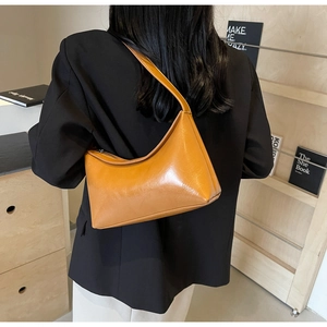Modern orange leather half-moon shoulder bag shown on a model in a minimalist setting