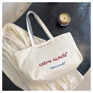Detail of embroidered Crème Glacée text and striped handle on white canvas tote bag