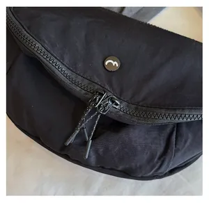 Close-up of smooth dual zippers and round logo detail on a black washed fabric crossbody bag