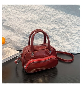 Detail of burgundy glossy leather handbag with silver rivets and sleek zipper pocket