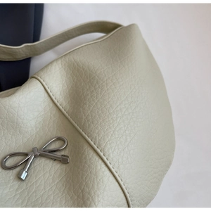 Close-up of beige pebble grain leather texture and silver metal bow on shoulder bag