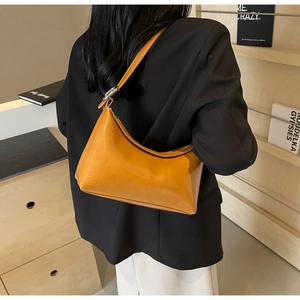 Detail of yellow PU leather shoulder bag with silver buckle worn over a black blazer