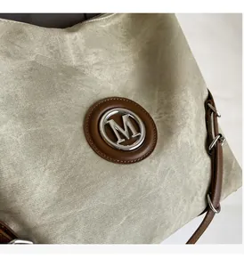 Detail of vintage beige canvas tote showing metallic M logo and brown leather trim