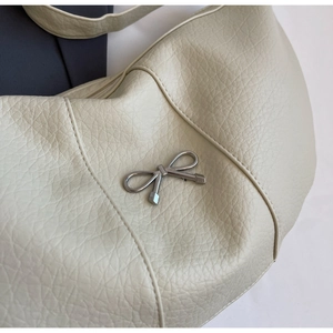 Close-up of creamy white lychee grain crescent bag with a silver metal bow charm
