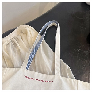 Detail of white canvas tote featuring red embroidery and blue striped handles