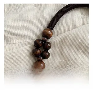 Detail of woven dark brown strap with smooth wooden beads and golden metal buckles