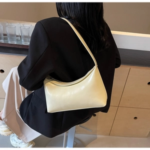 Lifestyle shot showing the cream crescent shoulder bag worn by a model in a warm room