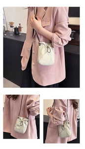 Detail of a cream canvas drawstring crossbody bag with black strap on a pink blazer
