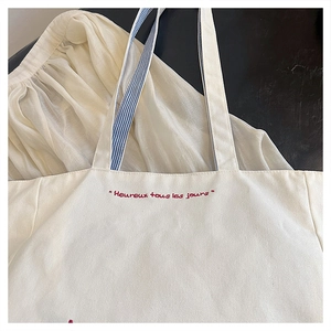 Detail of red French embroidery on textured canvas tote bag with striped straps