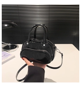 Detail of a black glossy patent leather mini handbag with dual handles and crossbody strap